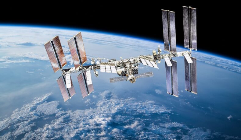 Stația Spațială Internațională, pe care vrea să o distrugă NASA, în orbita Pământului, cu planeta pe fundal și negru în conțul dreapta sus