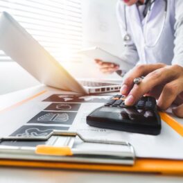 Doctor care folosește un calculator, în fața unui computer, pe un birou, similar cu calculatorul AI care poate prezice când mori